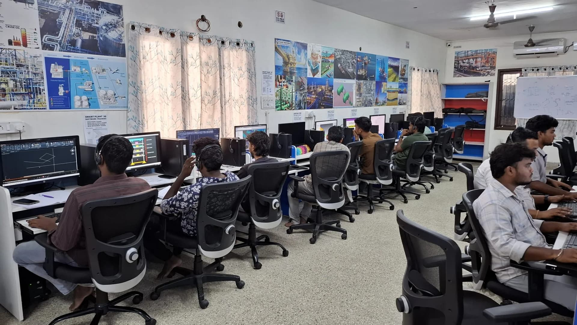 A computer lab full of students working at long desks with multiple monitors and keyboards.